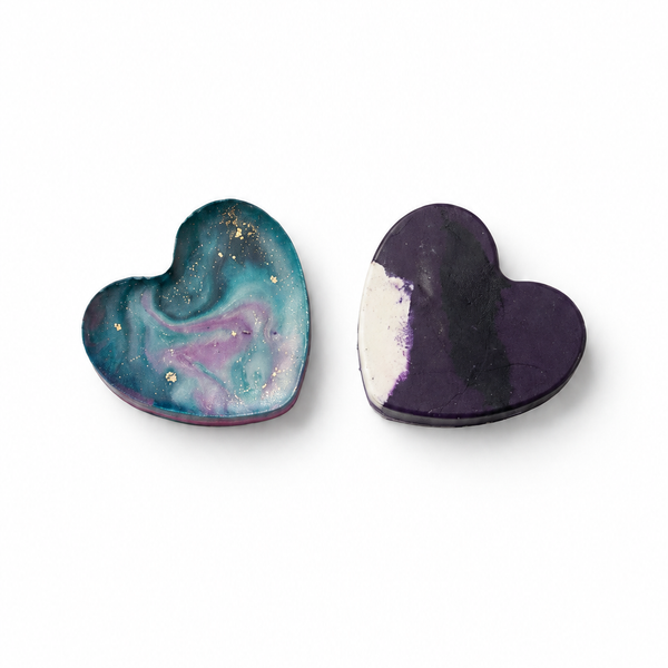 Two handmade heart-shaped Waxadoodle crayons with swirled multicolor patterns, centered on a pure white background